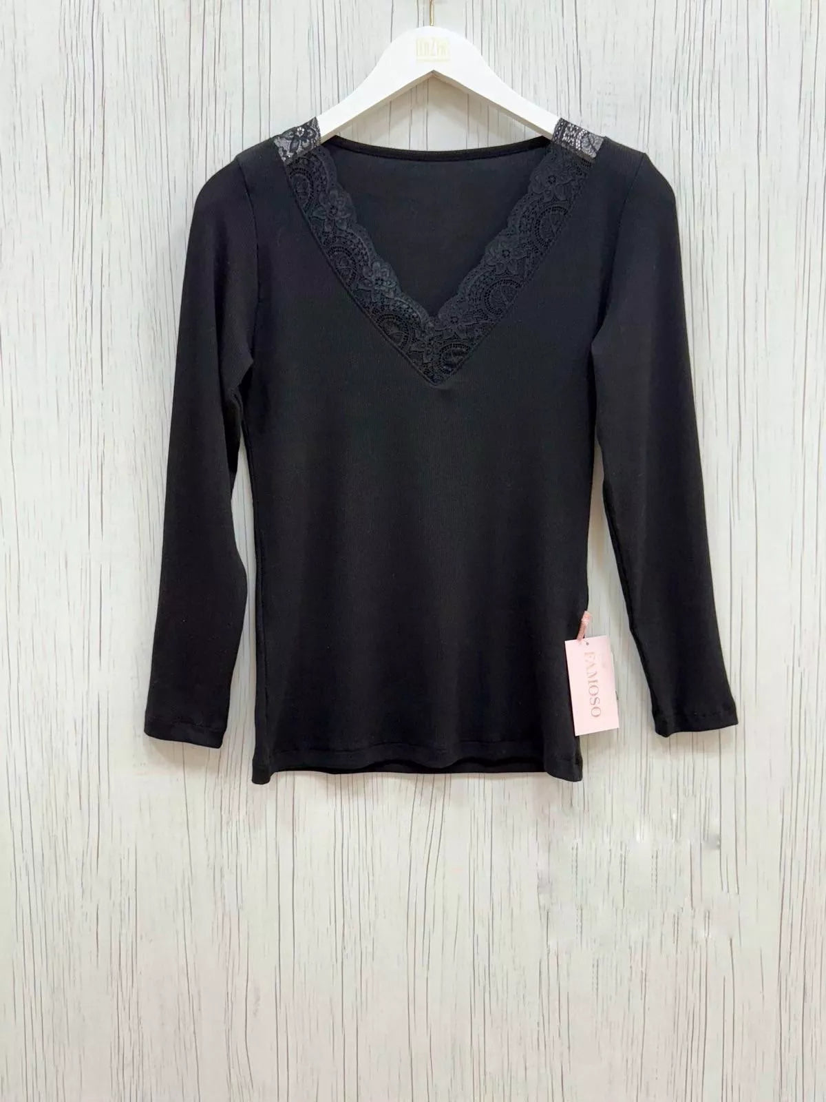 Black long-sleeve top with lace details on a hanger against a light wooden background