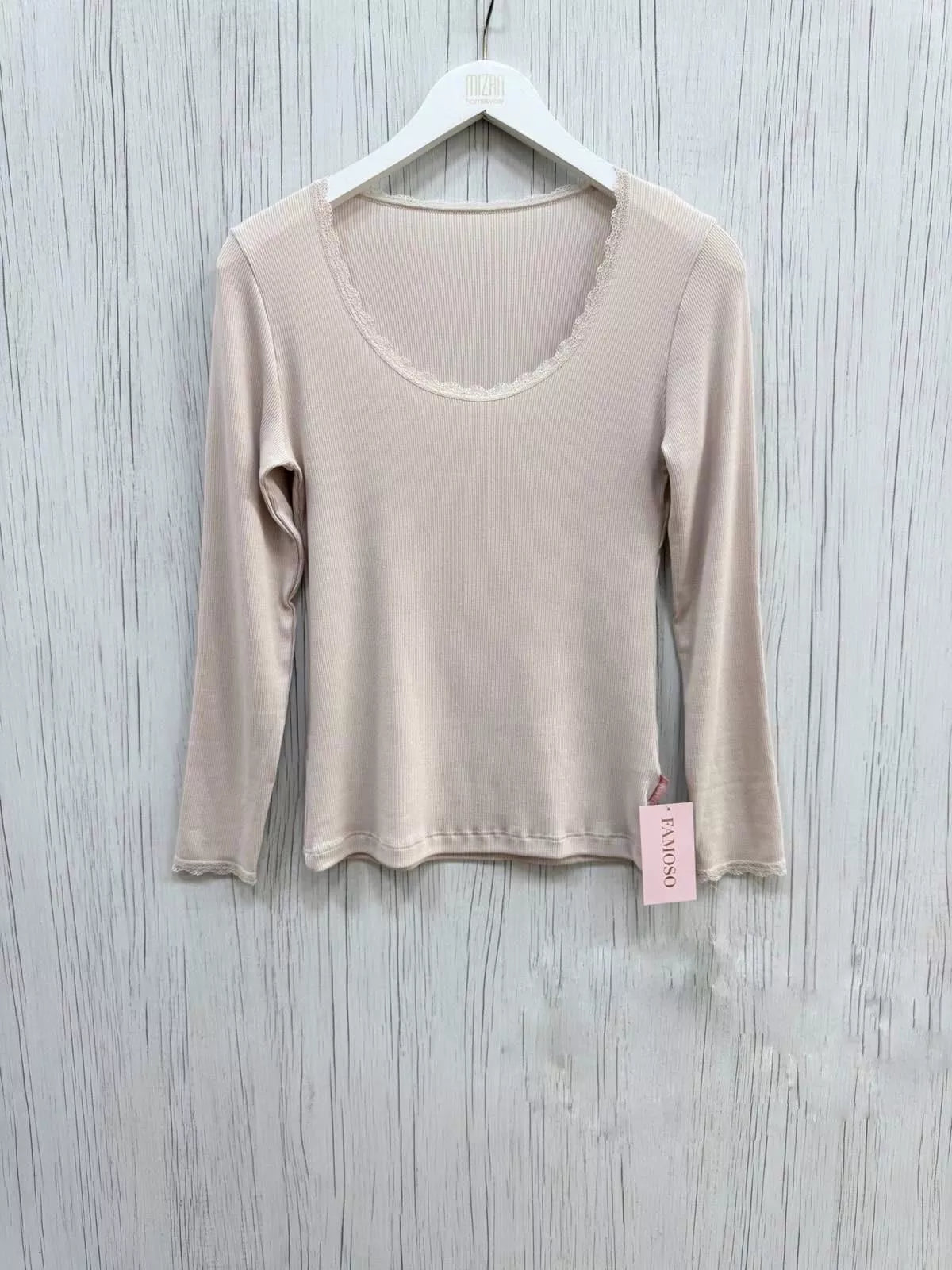 Beige long-sleeve top on a hanger with a visible tag against a light wooden background