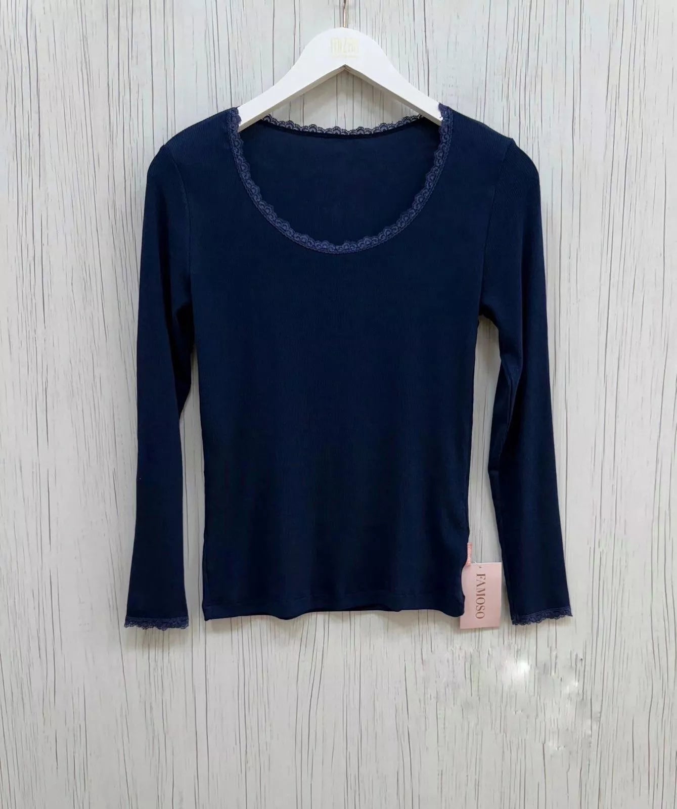 Navy long-sleeve top on a hanger with a visible brand tag against a light wooden background