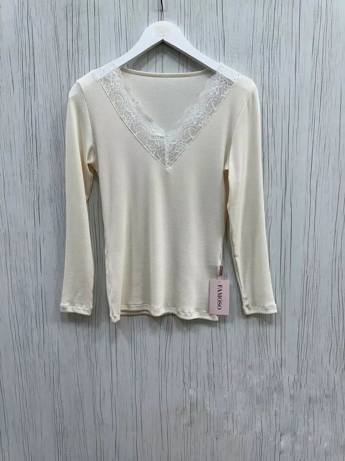 Beige long-sleeve top with lace detail on a hanger against a wooden background