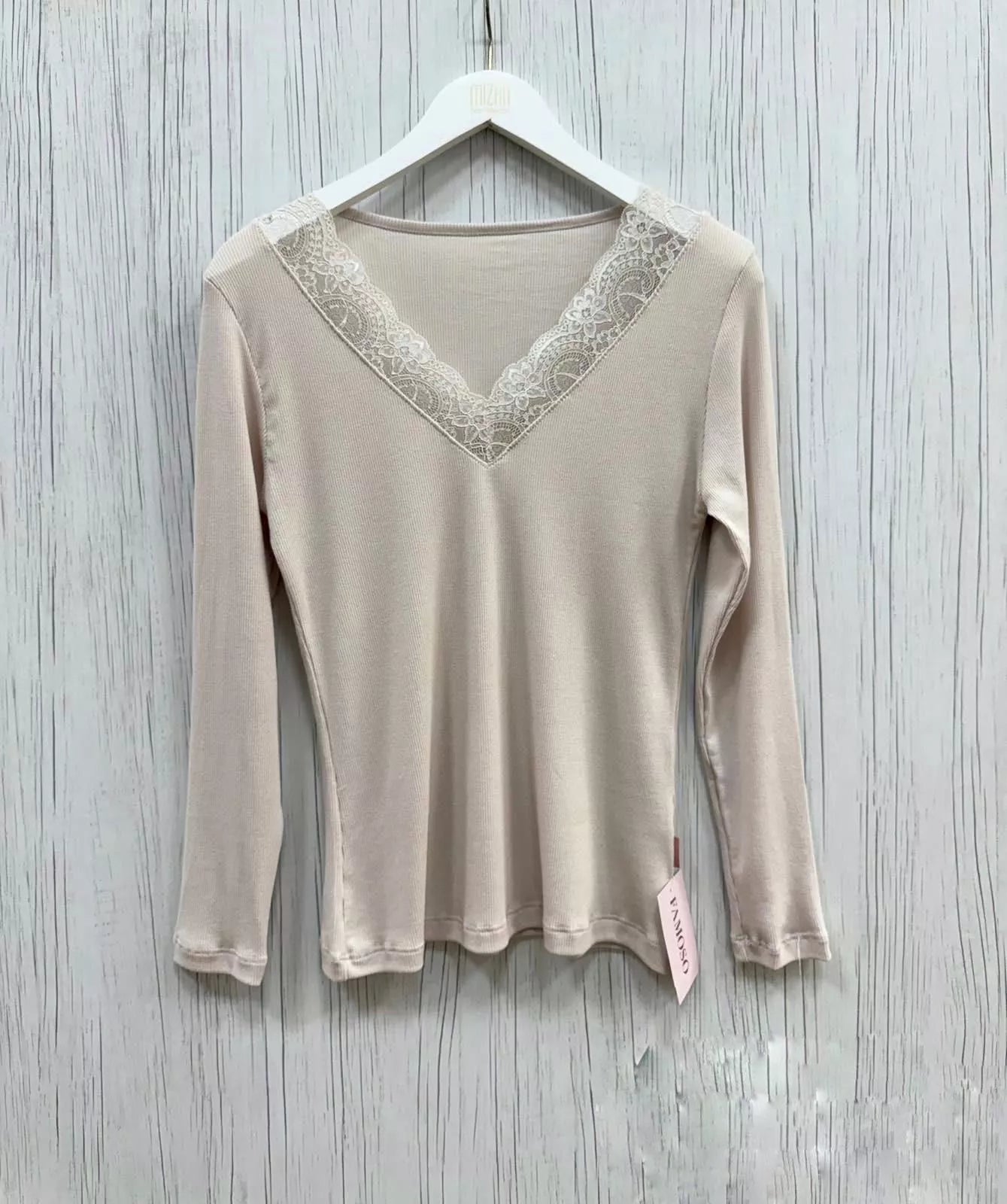 Beige long-sleeve top with lace detail on a hanger against a wooden background