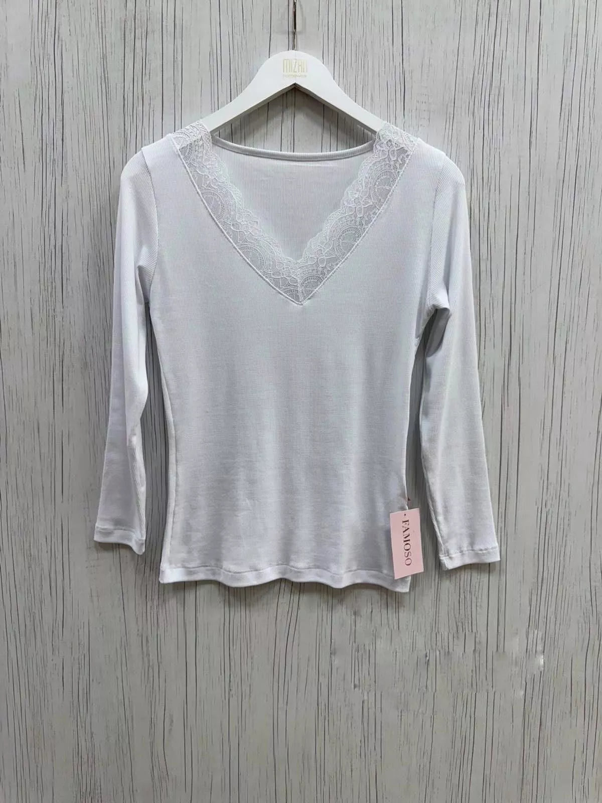 White long-sleeve top with lace detail on a hanger against a wooden background